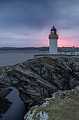  Kirkabister lighthouse stands on a rocky arch by the sea. Red sunset, blue sky. 