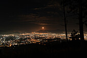 View of the Gulf of Naples at night, with city lights illuminating the coastline and reflecting on the calm waters.