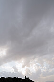 Scenic view of two lovers meeting on rocks by the sea, under a vast and moody sky.