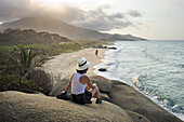 Woman sitting on a rock, admiring the beaches of Arrecifes, Tayrona National Natural Park, Department of Magdalena, Caribbean Region, Colombia, South America