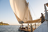 Einheimische auf Dahabeah Schiff unter Segeln, Passagier-Flussschiff der Lazuli-Flotte, auf dem Nil bei Sonnenuntergang, bei Assuan, Ägypten, Nordostafrika