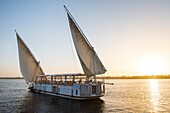 Dahabeah Schiff unter Segeln, Passagier-Flussschiff der Lazuli-Flotte, auf dem Nil bei Sonnenuntergang, bei Assuan, Ägypten, Nordostafrika