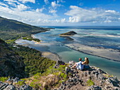  Aerial view of couple enjoying view over lagoon and coast halfway through hike up Le Morne mountain, Le Morne, Rivière Noire, Mauritius, Indian Ocean 