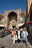  Iranische Frauen gehen am Qeysarie-Tor vorbei, dem Haupteingang zum Großen Basar von Isfahan auf dem Naqsh-e Jahan-Platz. Isfahan, Iran. 