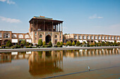 View of the Ali Qapu Palace and adjacent buildings reflected in a water pool in Naqsh-e Jahan Square, UNESCO World Heritage Site. Isfahan, Iran.