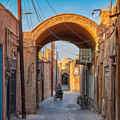 Ein Mann auf einem Motorrad fährt in einer Gasse durch einen Torbogen im historischen Viertel Fahadan in Yazd, Iran.