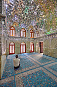  Ein Mann betet im Heiligen Schrein Ali Ibn Hamzeh, dessen Innenseite kunstvoll mit glänzenden Spiegelfliesen (Aina-Kari) verziert ist. Shiraz, Iran. 