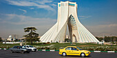 Yellow taxi passes by the Azadi Tower (Freedom Tower), an iconic landmark in Tehran, Iran.