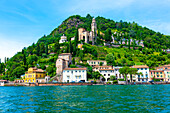 Haus und Kirche auf einer Bergkette an einem sonnigen Sommertag am Ufer, Luganersee in Morcote, Lugano, Tessin, Schweiz.