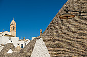  Trulli-Häuser mit der Kirche Santa Lucia im Hintergrund in Alberobello, Apulien, Italien. 