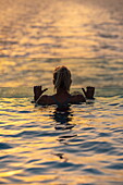  Silhouette of a woman relaxing on the edge of the infinity pool on the aft deck of the expedition cruise ship SH Diana (Swan Hellenic) at sunset, at sea, near Yemen, Middle East 