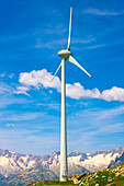 Wind Turbine and Mountain with Glacier and Against Blue Sky and Clouds in a Sunny Summer Day in Andermatt, Uri, Switzerland.