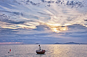 Vietnamese coracle fisherman pulls his net at sunrise. Hoi An, Quang Nam Province, Vietnam.