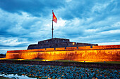 Vietnam national flag on top of the Flagtower of Imperial City illuminated at dusk. Hue, Vietnam.