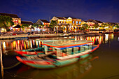  Boote auf dem Fluss Thu Bon und die in der Abenddämmerung beleuchtete Altstadt von Hoi An. Hoi An, Provinz Quang Nam, Vietnam. 