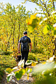 Schweden, Norrbottens län, Abisko, Nationalpark Abisko, Wanderer mit Hund auf Weg im Herbstwald