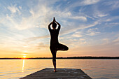  Woman doing yoga exercises on a jetty by the lake, yoga tree figure, Schleswig-Holstein, Germany 