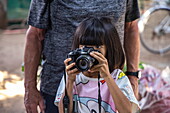  Young girl with squinting eyes looks through camera, Long Son, Phu Tan, An Giang, Vietnam, Asia 