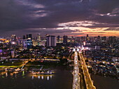  Aerial view of Chroy Changvar Bridge (also known as Cambodian-Japanese Kizuna Friendship Bridge) and river cruise ship RV Mekong Discovery anchored on Tonle Sap River with city skyline at dusk, Daun Penh District, Phnom Penh, Cambodia, Asia 