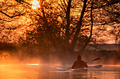  Kayakers on Spreewald stream, paddlers riding in the fog and sunrise, Spreewald stream, stream, spring, foggy landscape, golden hour, river landscape, winter paddling, paddling, UNESCO biosphere reserve, Spreewald, local recreation area, Brandenburg, Germany\n 