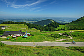  Woman mountain biking past alpine pasture, Schlechtenbergalm, Kampenwand, Chiemgau Alps, Upper Bavaria, Bavaria, Germany 