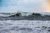 Waves crashing in a turbulent sea under a cloudy sky, creating a dynamic and powerful scene.