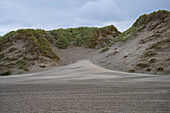 A serene landscape featuring sand dunes covered with grass under a cloudy sky.