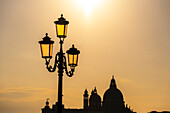 Lamp post with golden sky in Venice, Italy, with a silhouette of the Basilica di Santa Maria della Salute in the background.