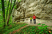  Man and woman hiking under a rock face, Klararuh, Streitberg, Wiesenttal, Franconian Switzerland, Franconia, Bavaria, Germany 