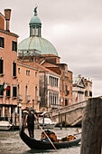 A gondolier passes through a Venetian canal, with the flag of Italy in the background, Venice Italy