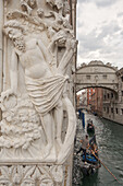 A gondolier rows his boat down a canal in central Venice, Italy with relief of building decorations visible