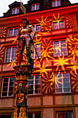 Fountain with Statue in Front of an Illuminated House in Old Town in a Dusk in City of Neuchatel, Canton Neuchatel, Switzerland.