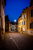 Cobblestone Street in Old Town with Illuminated House and Window in Dusk in City of Neuchatel, Canton Neuchatel, Switzerland.