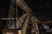  Nighttime view of the illuminated Ponte Luiz I bridge from the north bank. Birds in the night sky, Porto, Portugal 
