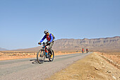 Mountain biker with electric assistance on a straight road through the reg, from Agdz to Zagora, Draa River valley, Province of Zagora, Region Draa-Tafilalet, Morocco, North West Africa