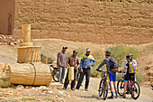 Mountain bike riders meeting bamboo basket maker in a village on the road from Agdz to Zagora, Draa River valley, Province of Zagora, Region Draa-Tafilalet, Morocco, North West Africa