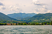 Häuser am Ufer und Bergkette am Luganersee in Caslano, Tessin, Schweiz.