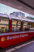 Railroad Station and Red Bernina Express Train and a Luxury Hotel in a Cloudy Summer Day in Engadin, Maloja, St Moritz, Grisons, Switzerland,