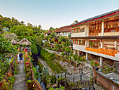 Houses along a narrow alleyway surrounded by lush tropical greenery in Ubud, Bali, Indonesia.