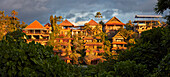Panoramic view of residential houses surrounded by lush greenery and lit by rising sun in Ubud, Bali, Indonesia.