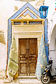  Traditional house with ornate historic wooden door with Arabic mosaic frieze and woven carpets on the house wall for sale in Hammamet, Tunisia 