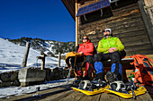  Man and woman hiking with snowshoes taking a break at an alpine hut, at Trainsjoch, Mangfall Mountains, Tyrol, Austria 