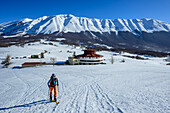 Frau auf Skitour steigt zum Monte Mileto auf, Monte Amaro im Hintergrund, Nationalpark Majella, Apenninen, Abruzzen, Italien