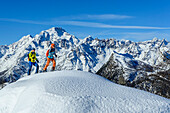  Man and woman on ski tour ascending to Rifugio Cristina, Monte Disgrazia in the background, Alpe Prabello, Bernina Range, Lombardy, Italy 