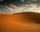 Lone figure stands on sand dunes at sunset on the edge of the Sahara at Erg Chebbi near Merzouga in Southern Morocco