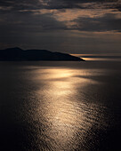 The sun sets behind clouds over Myrtou bay on the west coast of Kefalonia
