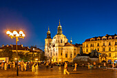 Die barocke St.-Nikolaus-Kirche und das Jan-Hus-Denkmal auf dem Platz Altstädter Ring in der Abenddämmerung, Prag, Tschechische Republik