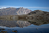  Passengers of an expedition cruise ship are reflected in the still waters of a lake with distant mountains near Sirius Station, Ella Island, Arctic Greenland, Europe 