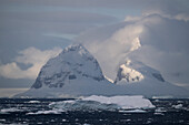  The late afternoon sun bathes a scene of icebergs, mountains and low-hanging clouds near one of the continent&#39;s highlights, the Lemaire Channel, Antarctic Peninsula, Antarctica 