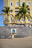 Frau in gelbem Kleid betrachtet einen Marien Altar am Strand Playa La Canteras, Hauptstadt Las Palmas de Gran Canaria, Kanarische Inseln, Spanien, Europa